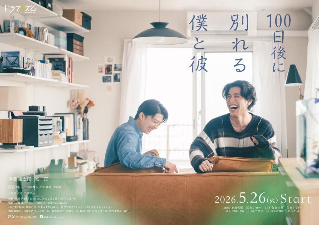Two men laughing at a desk in a bright, cozy room with shelves and office items in the background, Japanese poster text overlaid on the right side.