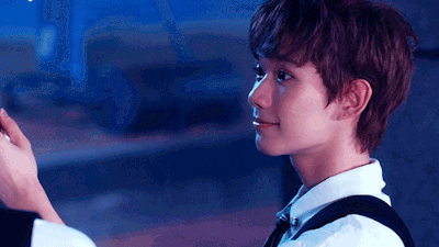 Profile of a young man in a white shirt and bow tie, looking to the left under blue stage lighting.