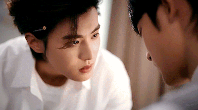 Close-up of a woman in a white shirt leaning toward a man, both looking intently at each other in a softly lit scene.